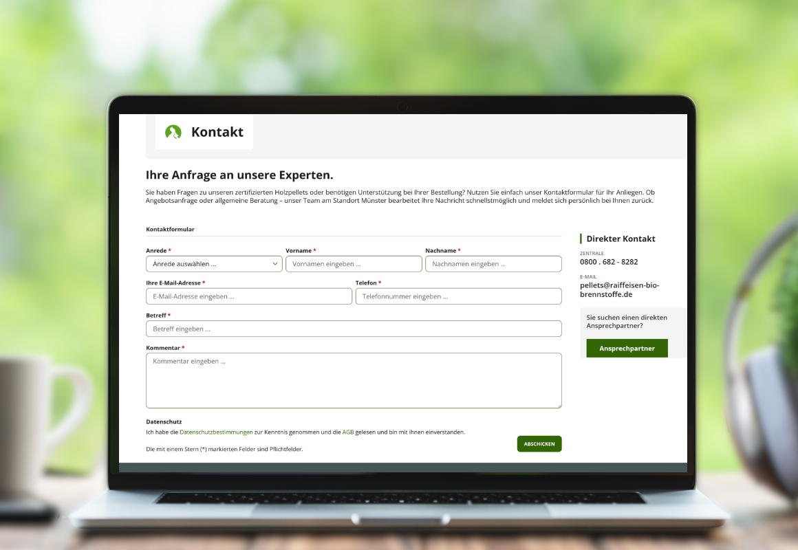Arbeitsplatz mit Laptop auf welchem das Kontaktformular geöffnet ist, Kaffeetasse und Pflanze auf einem Holzschreibtisch – moderne Arbeitsplatzszene in der Frontansicht.