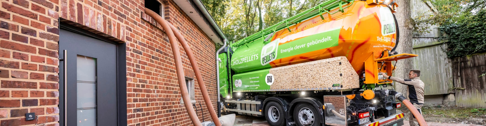 Silofahrzeug liefert Holzpellets in den Lagerraum eines Wohnhauses. Zwei Förderschläuche verbinden den Pellet-Lkw mit dem Gebäude während der Einblasung der Pellets.