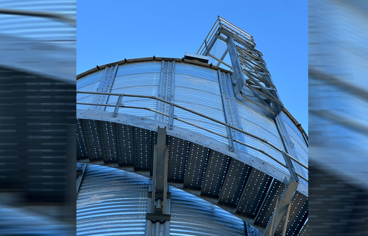 Nahaufnahme eines großen metallenen Lagersilos mit Treppe und Plattform vor blauem Himmel.