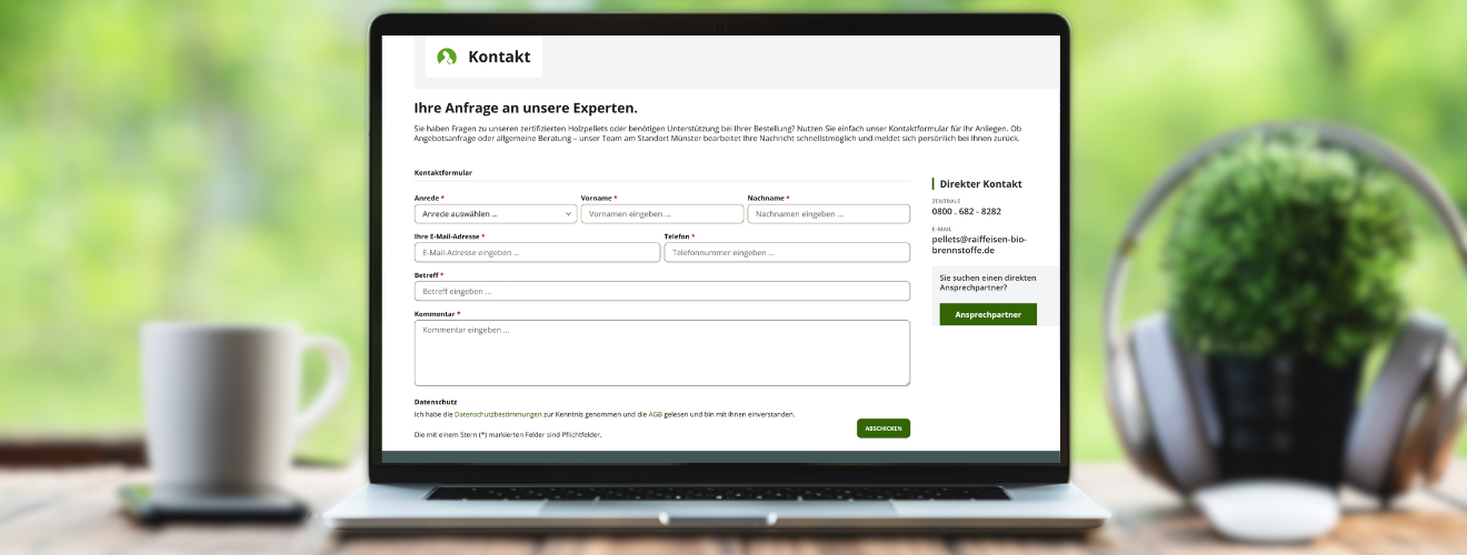 Arbeitsplatz mit Laptop auf welchem das Kontaktformular geöffnet ist, Kaffeetasse und Pflanze auf einem Holzschreibtisch – moderne Arbeitsplatzszene in der Frontansicht.