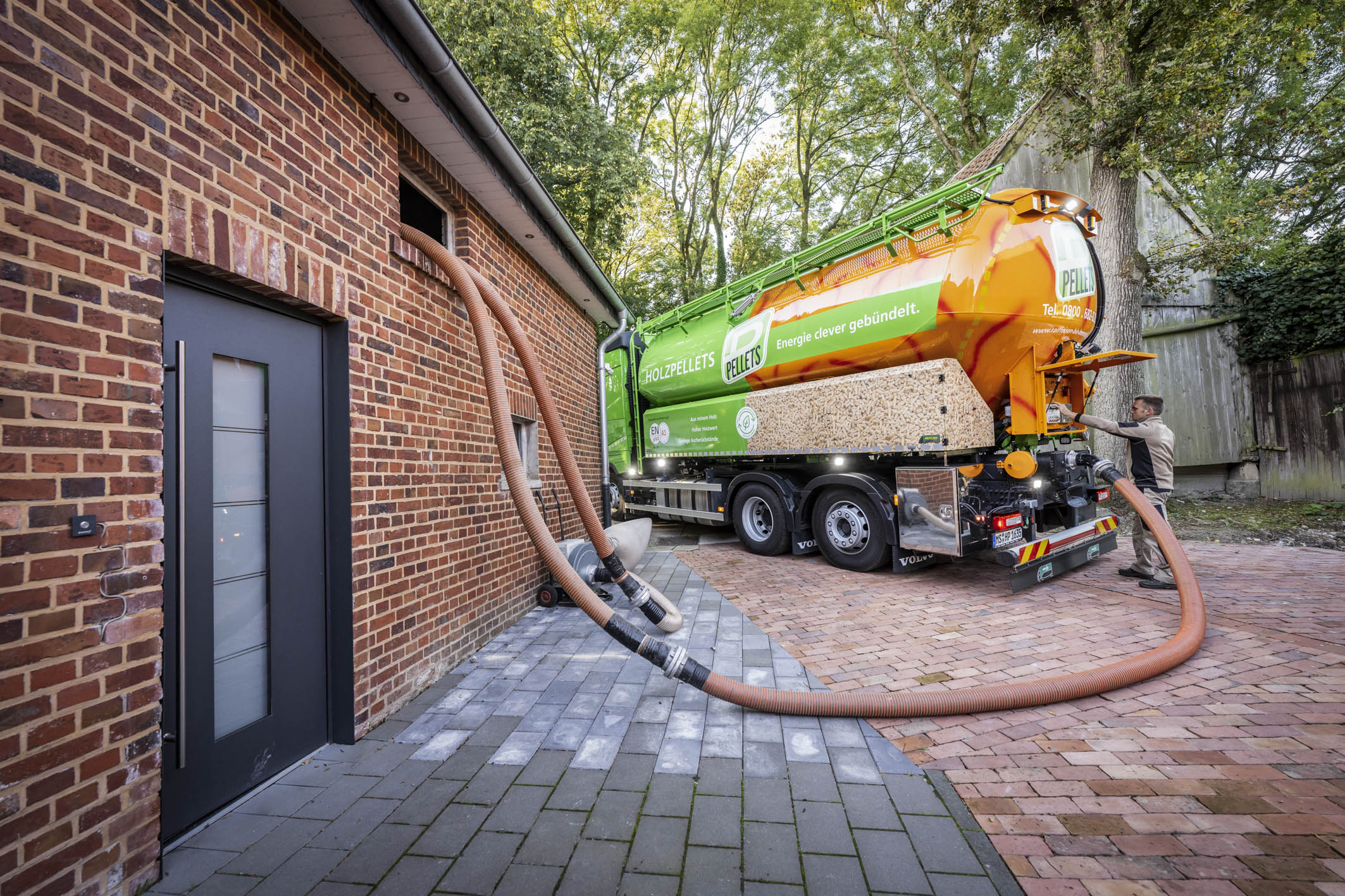Foto eines Pellet Tankwagens, der per Schlauch Pellets in ein Wohnhaus bläst