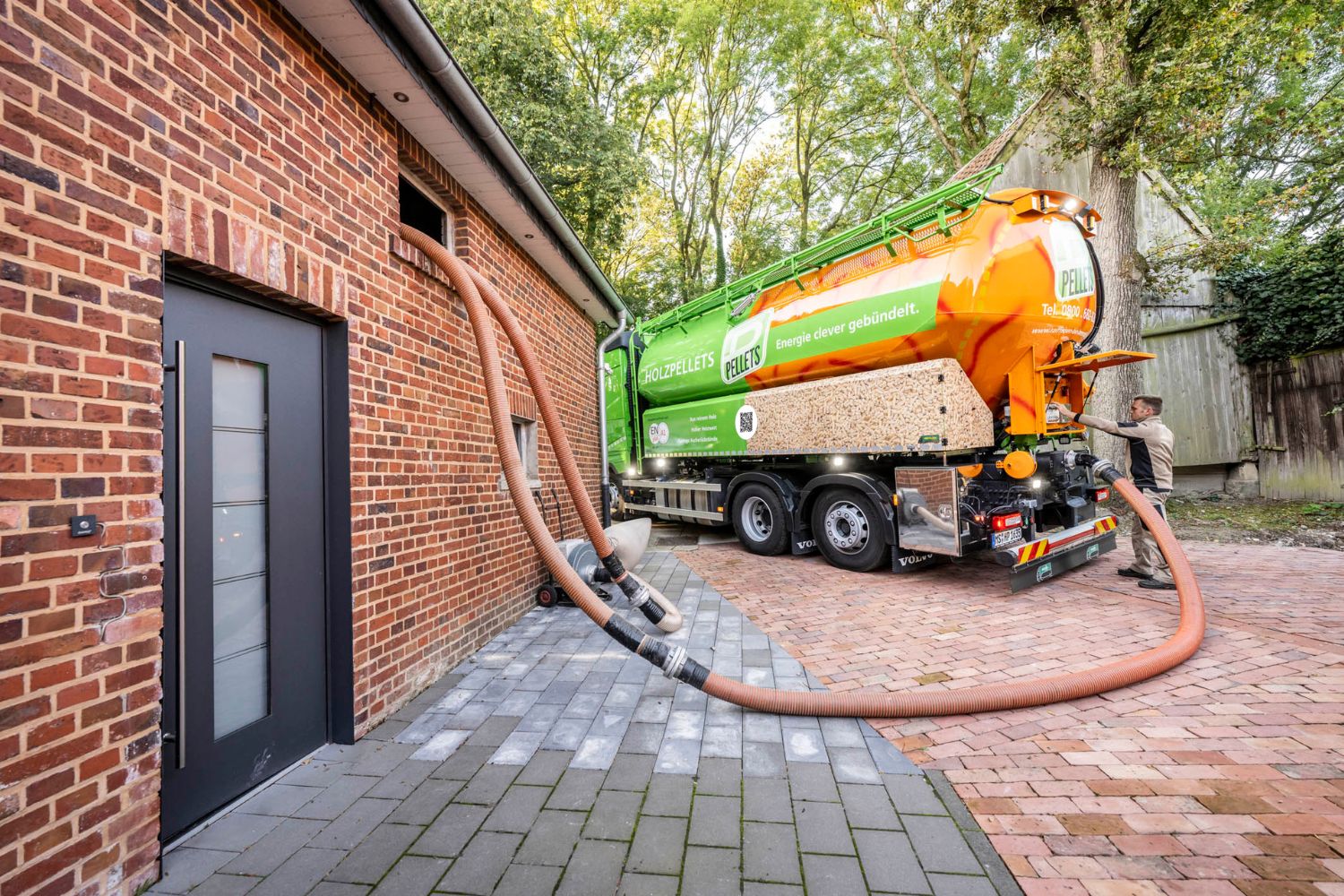 Foto eines Pellet Tankwagens, der per Schlauch Pellets in ein Wohnhaus bläst