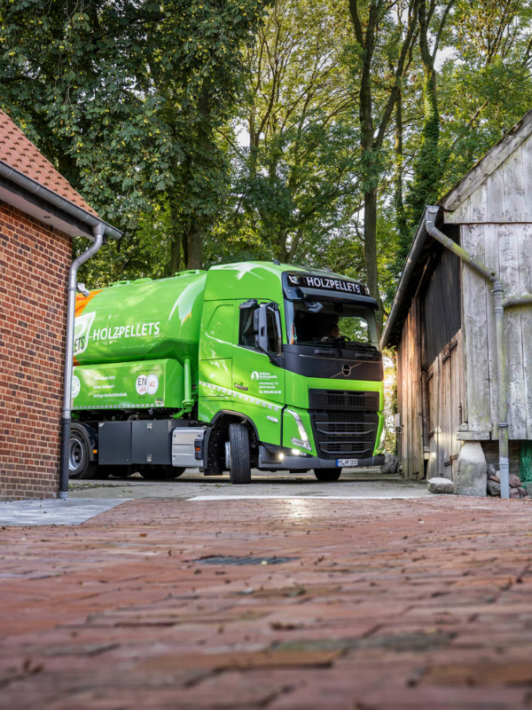 Ein grüner Pellet-LKW der Raiffeisen Bio-Brennstoffe fährt einen Hof an und bereitet die Anlieferung vor.