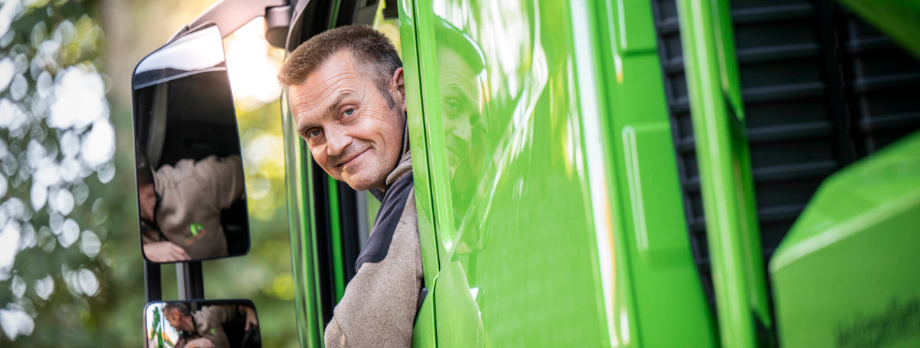 Lächelnder LKW-Fahrer schaut aus dem Fenster eines grünen RBB-LKWs.